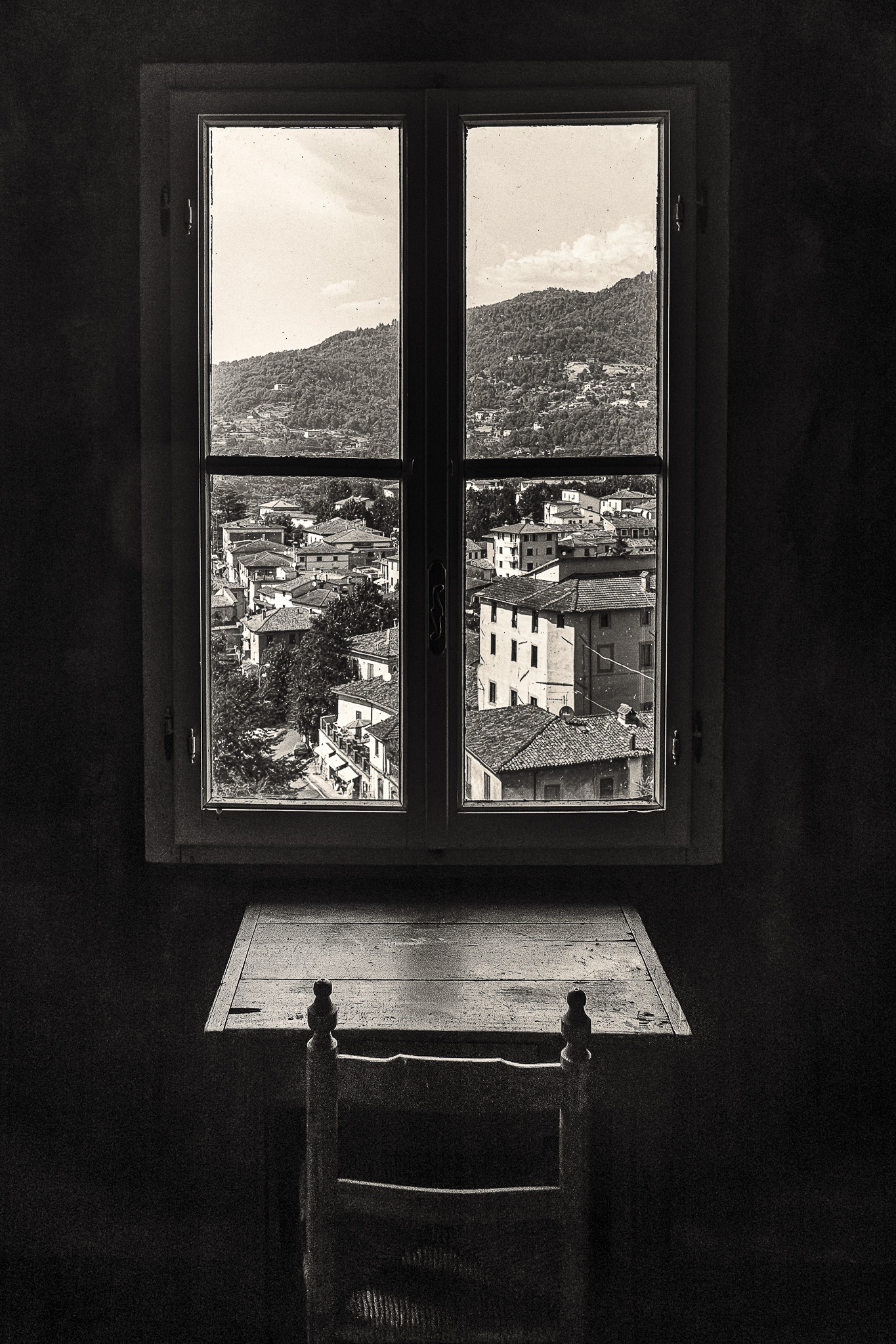 Black and white image of a table and chair at window